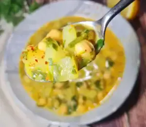 Cuchara con una porción de One-Pot Chickpea Potato Curry Soup: garbanzos, patatas y trocitos de espinaca.