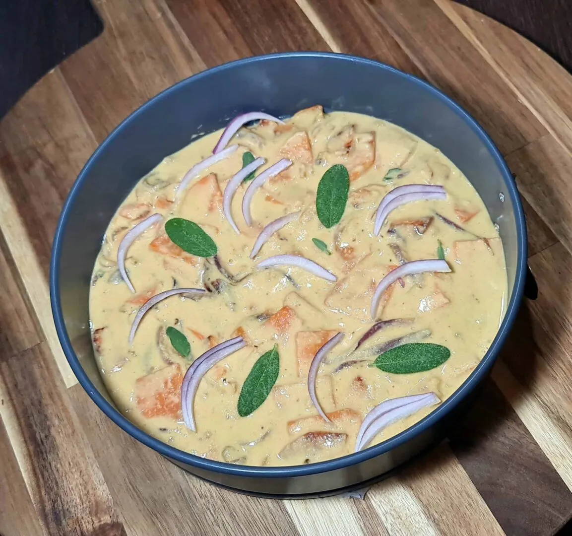 Springform pan filled with chickpea batter, sweet potato cubes, red onion slivers, and sage leaves.