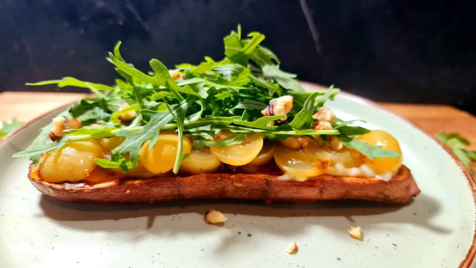 Side-angle of loaded sweet-potato toast showing layers of roasted grape halves, yogurt, arugula and nut crumble.
