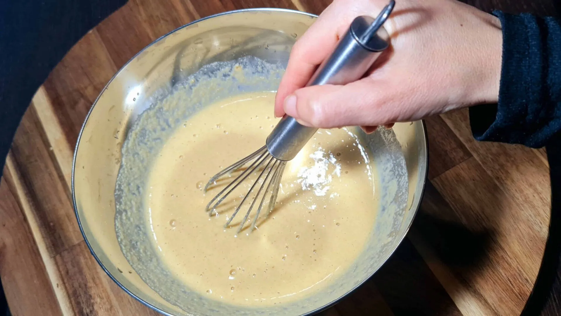 Hand whisking smooth chickpea flour batter in a metal bowl for vegan sweet potato frittata.