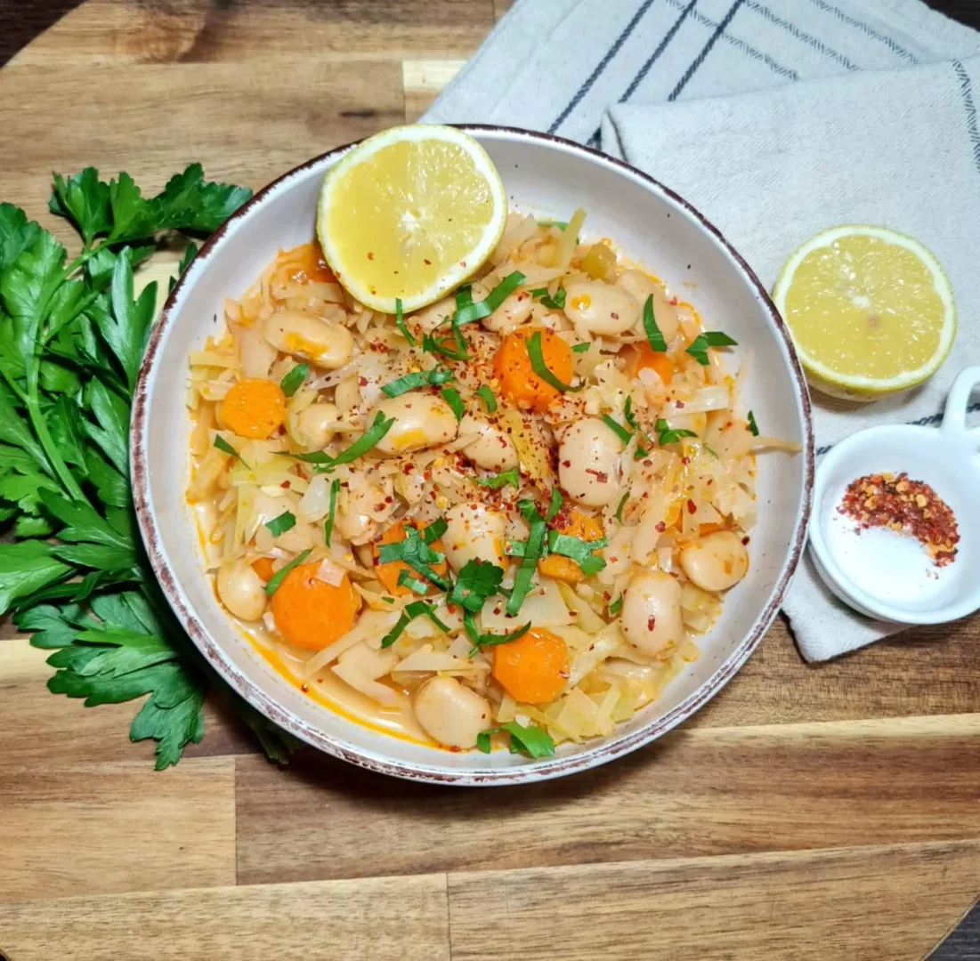 Overhead view of cabbage bean soup in rustic bowl with parsley and lemon halves