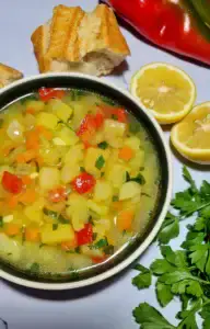 A close-up, overhead view of a bowl of chunky easy vegan potato soup with visible diced potatoes, carrots, and red peppers, garnished with parsley.