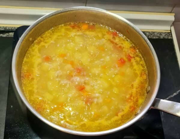 The easy vegan potato soup is visibly thickening and simmering on the stovetop, turning into a rich, creamy-textured soup.