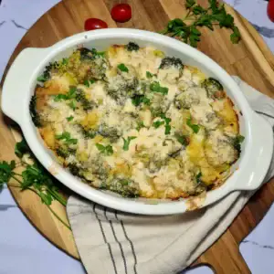 A freshly baked vegan broccoli potato casserole in a white dish, with a golden-brown, crispy topping and a spoon taking a scoop out to show the creamy interior.