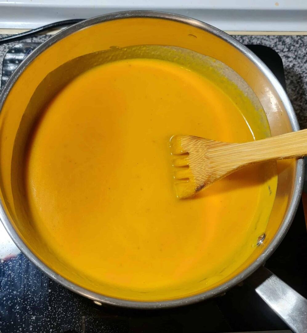 A pot of perfectly smooth, bright orange carrot ginger soup being stirred with a wooden spatula after blending.
