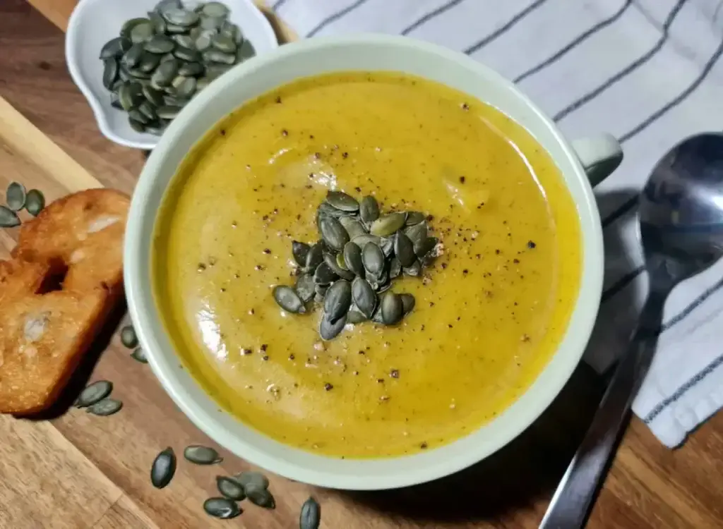 Top view of creamy pumpkin zucchini soup no cream garnished with pumpkin seeds and black pepper.