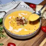 A close-up bowl of silky winter kohlrabi soup, topped with golden crispy kohlrabi cubes and a swirl of coconut cream. A hand lifts a spoonful to show its smooth, velvety texture.