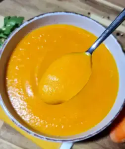 A bowl of creamy carrot soup with a spoon showing its smooth and velvety texture