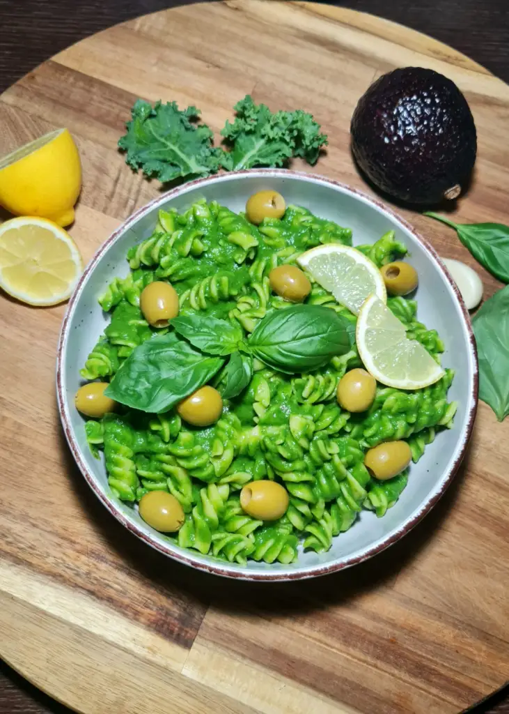 A hearty serving of gluten-free avocado green pasta garnished with fresh basil leaves and green olives.
