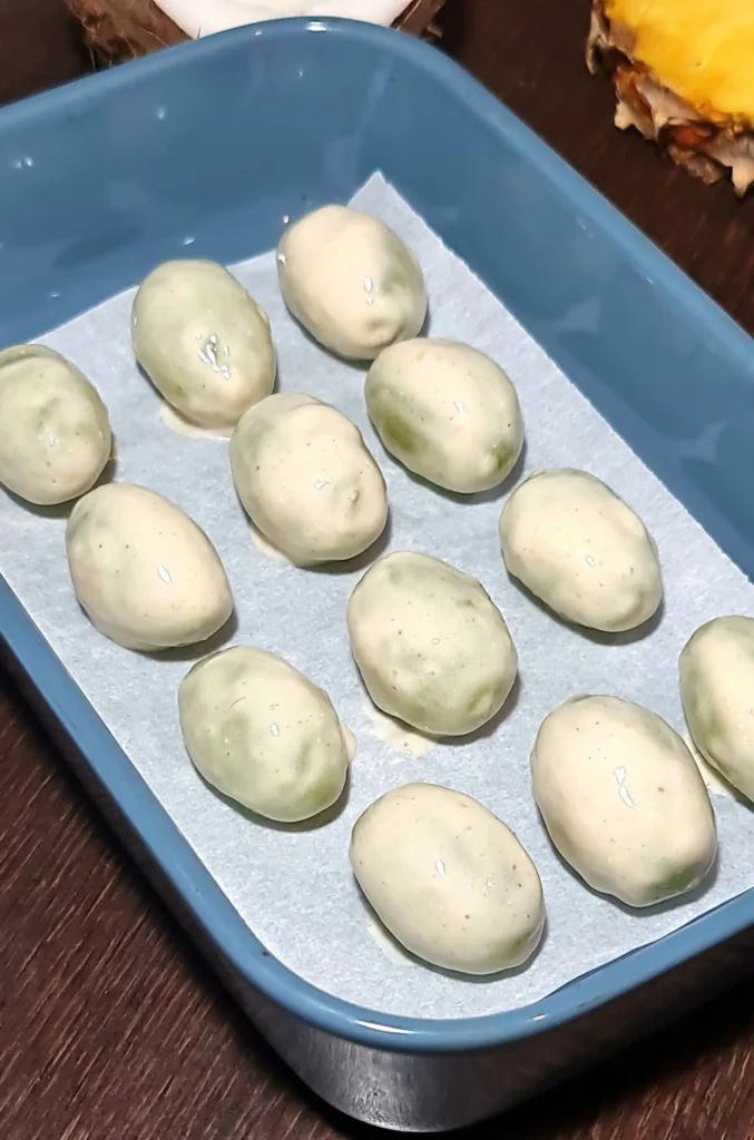 White yogurt-coated grapes arranged neatly on parchment paper inside a blue dish, a crucial step for chocolate grape bark.