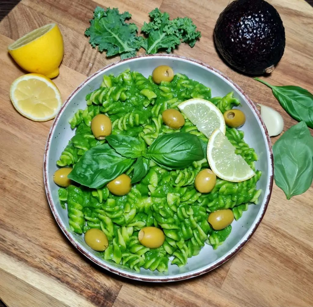 Close-up of gluten-free avocado green pasta with fresh garnish on a wooden table.