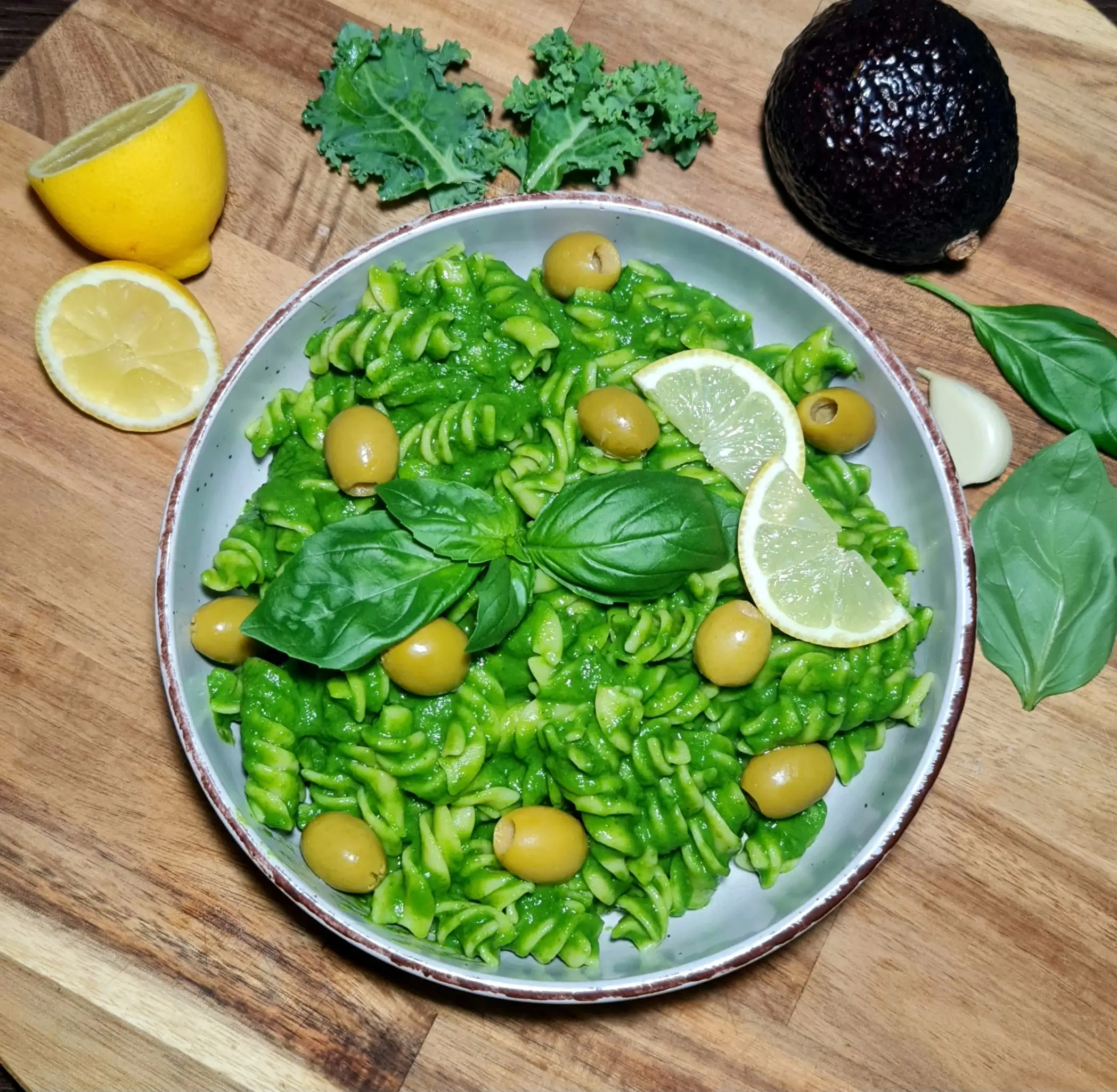 Close-up of gluten-free avocado green pasta with fresh garnish on a wooden table.