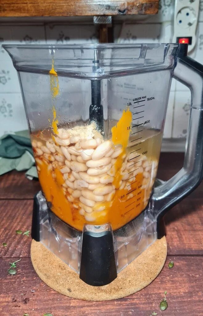 Pumpkin puree, white beans, and vegetable broth in blender pitcher ready to blend into creamy soup, showing easy one-step preparation on wooden table with cork trivet