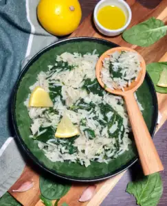 A beautifully styled serving of spinach rice in a green bowl, garnished with lemon slices and accompanied by fresh ingredients in the background.