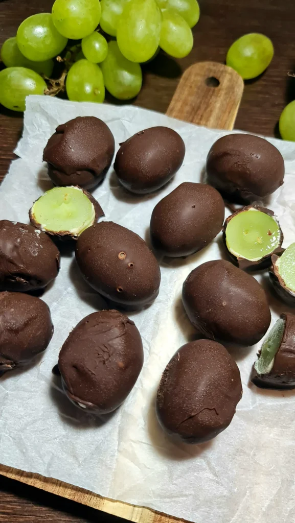 An overhead close-up of dark chocolate grape bark bites on parchment paper, showing the halved grapes with their green center.