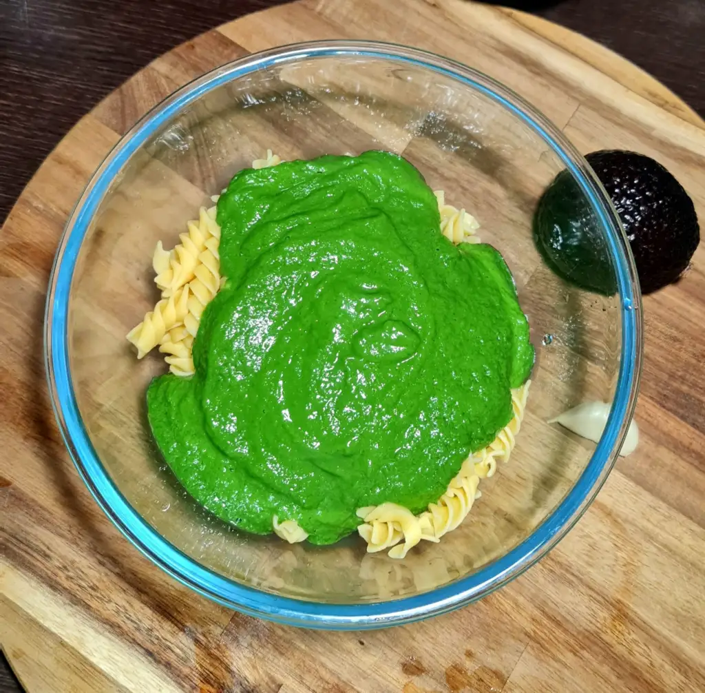 Glass bowl with cooked fusilli topped with a thick, vibrant sauce to create a gluten-free avocado green pasta.