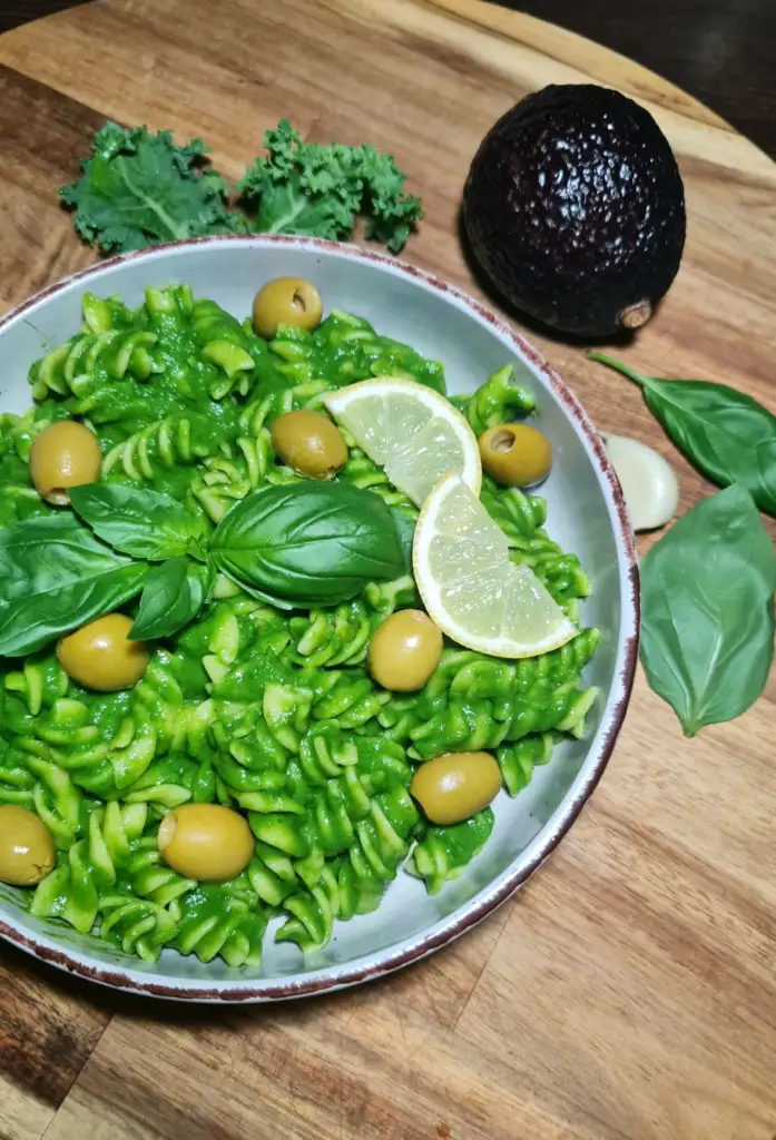 Angled view of a plate of gluten-free avocado green pasta served on a wooden board with raw ingredients.