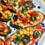 Macro shot of 5-Ingredient Mediterranean Baked Sweet Potatoes, detailing the creamy sauce draped over spiced chickpeas, fresh tomatoes, and black olives.