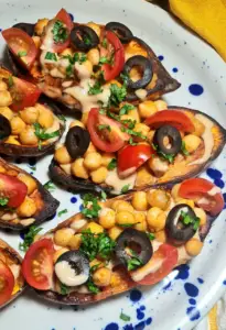 Macro shot of 5-Ingredient Mediterranean Baked Sweet Potatoes, detailing the creamy sauce draped over spiced chickpeas, fresh tomatoes, and black olives.