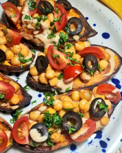 Macro shot of 5-Ingredient Mediterranean Baked Sweet Potatoes, detailing the creamy sauce draped over spiced chickpeas, fresh tomatoes, and black olives.