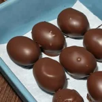 A tray of smooth, dark chocolate-covered grapes arranged on parchment paper for the high protein chocolate yogurt grapes.