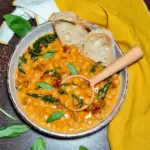 A wooden spoon scooping up a hearty portion of creamy Merry me chickpeas from a garnished bowl with crusty bread.