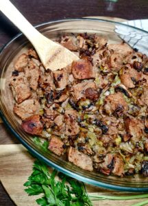 A glass baking dish filled with golden-brown baked vegan stuffing, with a wooden spoon resting inside.