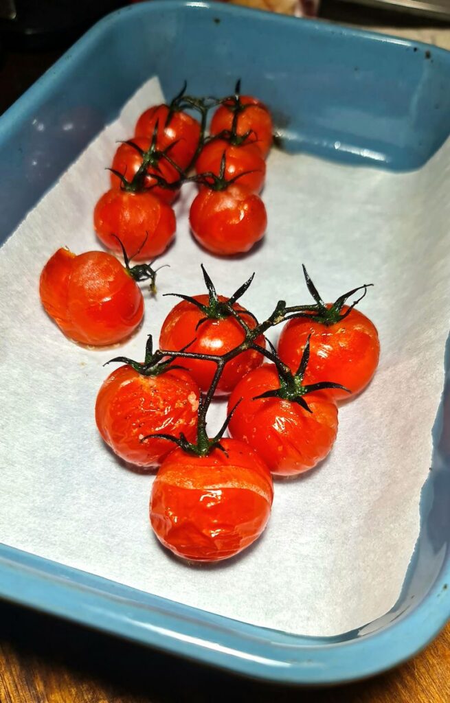Oven-roasted, blistered cherry tomatoes on the vine in a blue dish, a juicy topping for a roasted vegetable quinoa bowl.