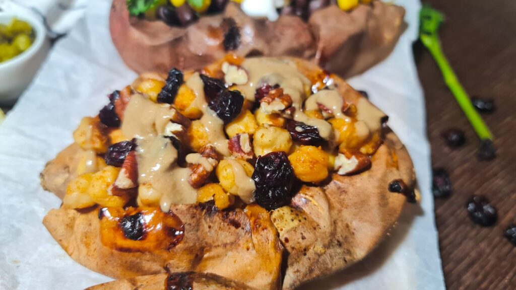 Close-up of vegan stuffed sweet potatoes topped with roasted chickpeas, pecans, dark raisins, and tahini.