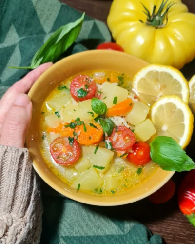 A person wearing a warm knitted sweater holding a yellow bowl of freshly made potato rice soup.
