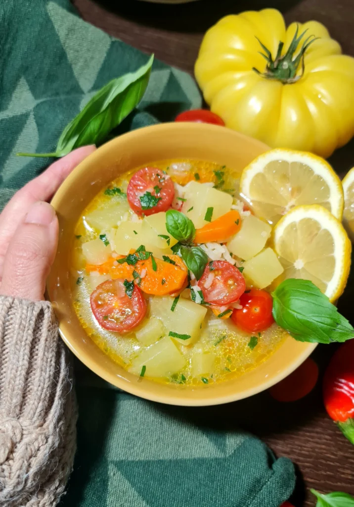 A person wearing a warm knitted sweater holding a yellow bowl of freshly made potato rice soup.