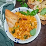 A detailed view of a bowl filled with Merry me beans, showing the creamy orange sauce, white beans, spinach, and sun-dried tomatoes.