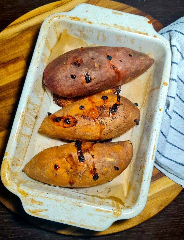 Three freshly baked vegan stuffed sweet potatoes base in a white ceramic dish.
