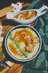 Dark and moody food photography featuring a bowl of mashed potatoes with vegan mushroom gravy and a filled gravy boat.