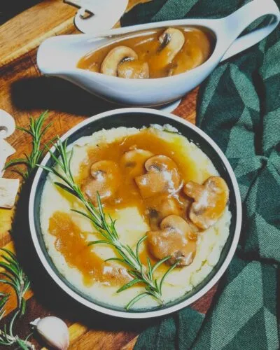 Dark and moody food photography featuring a bowl of mashed potatoes with vegan mushroom gravy and a filled gravy boat.