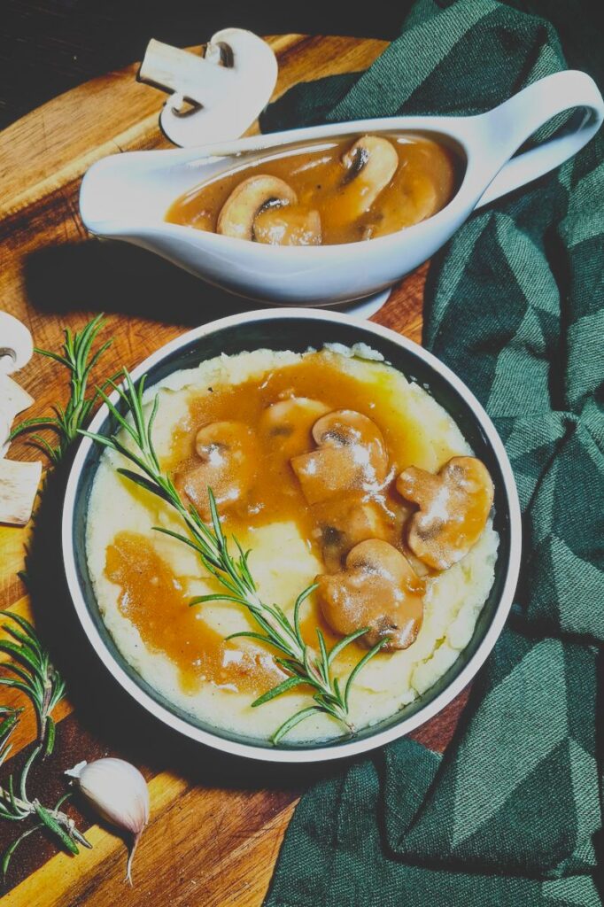 Dark and moody food photography featuring a bowl of mashed potatoes with vegan mushroom gravy and a filled gravy boat.