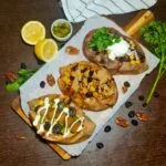 A wooden board displaying three different variations of vegan stuffed sweet potatoes horizontally.