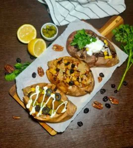 A wooden board displaying three different variations of vegan stuffed sweet potatoes horizontally.