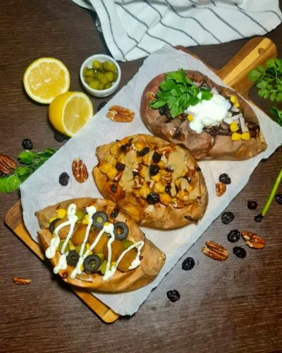 A wooden board displaying three different variations of vegan stuffed sweet potatoes horizontally.