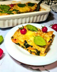 A thick slice of vegan pumpkin spinach lasagna served on a white plate, showing vibrant layers of orange squash and green leaves.