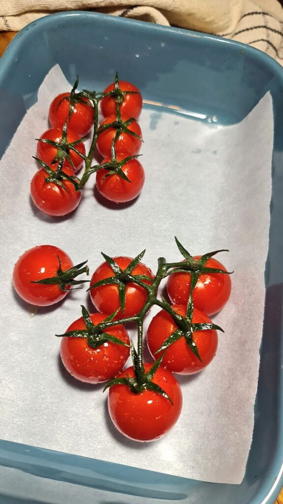 Top-down view of raw cherry tomatoes on the vine in a blue dish to accompany a roasted vegetable quinoa bowl.