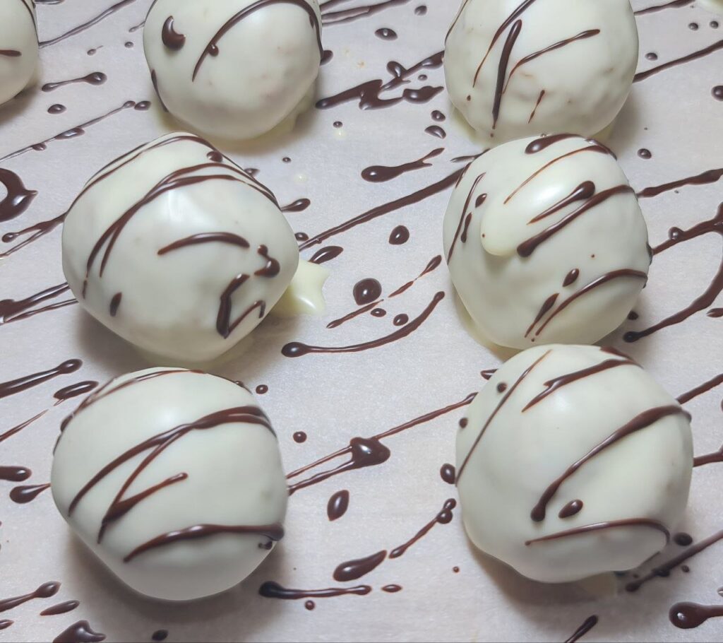 A batch of white chocolate-coated truffles drizzled with dark chocolate, resting on a sheet of parchment paper.