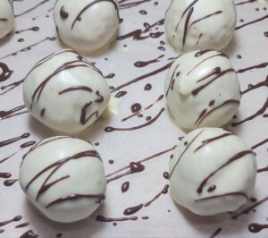 A batch of white chocolate-coated truffles drizzled with dark chocolate, resting on a sheet of parchment paper.