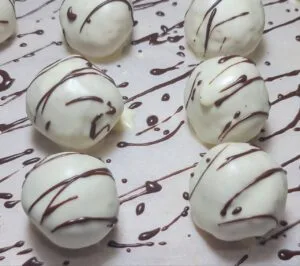 A batch of white chocolate-coated truffles drizzled with dark chocolate, resting on a sheet of parchment paper.