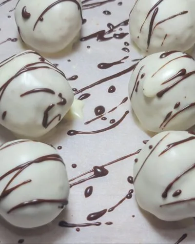 A batch of white chocolate-coated truffles drizzled with dark chocolate, resting on a sheet of parchment paper.