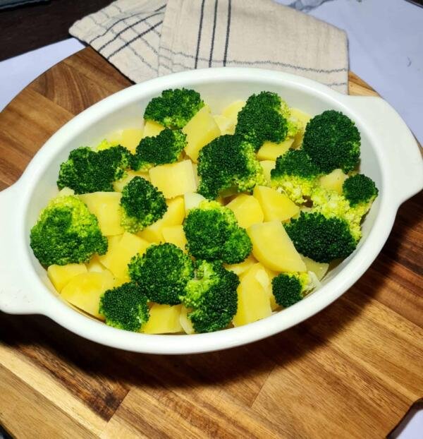 A white oval baking dish filled with cooked potato chunks and fresh broccoli florets, ready to be topped with sauce and baked.