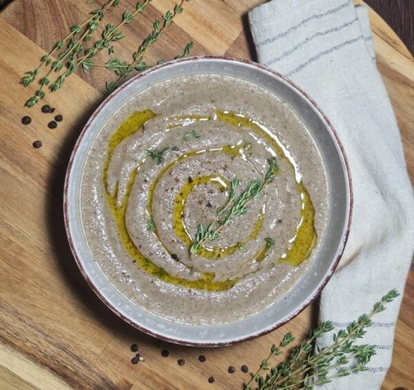 A bowl of creamy mushroom soup beautifully garnished with an olive oil swirl and a fresh sprig of thyme on a wooden cutting board.