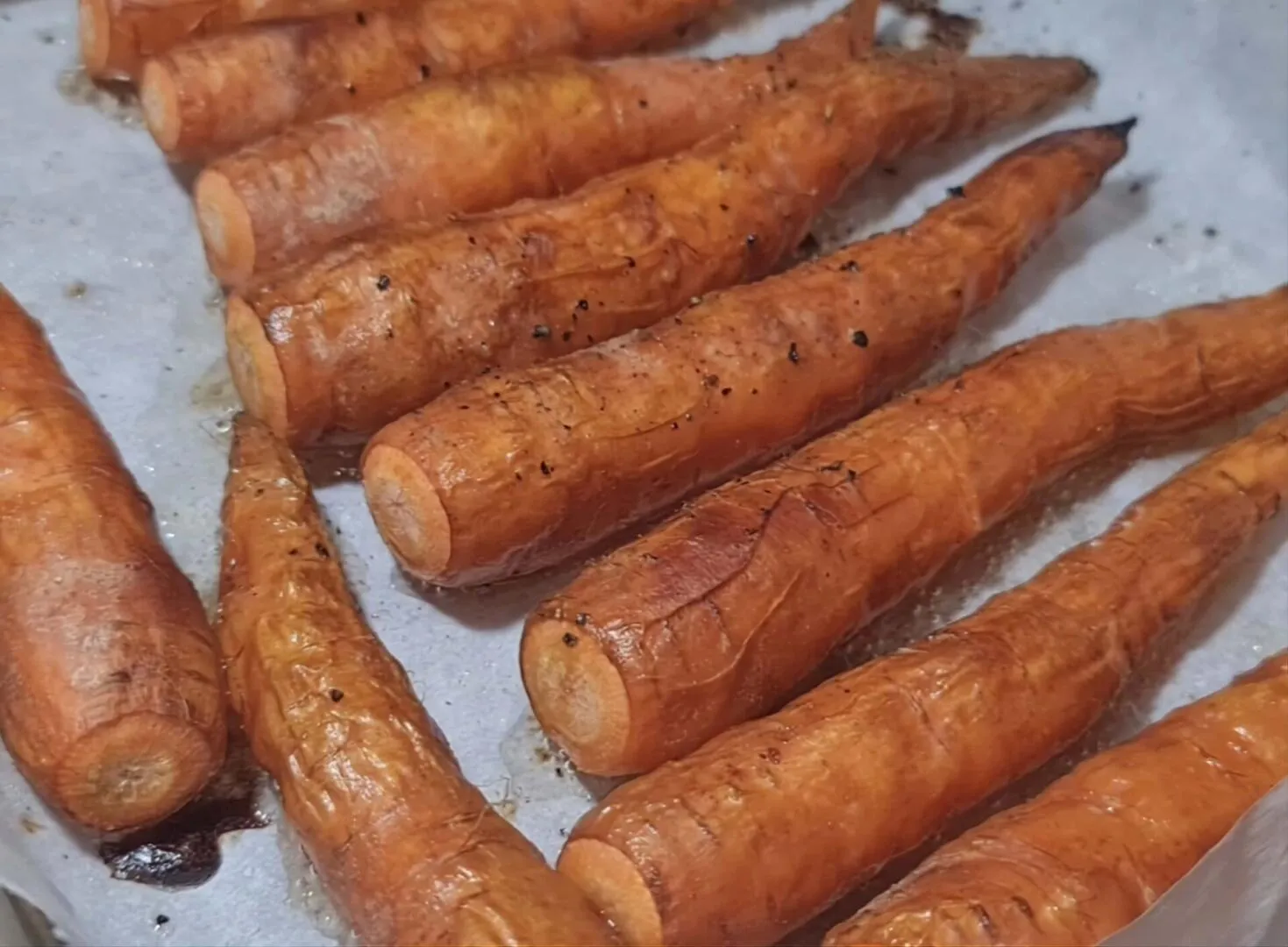 A close-up macro shot of whole carrots fresh from the oven, showing their roasted, caramelized, and slightly wrinkled skin.