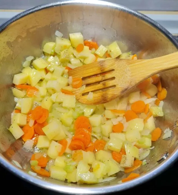 Diced potatoes, carrots, and onions cooking together in the pot, ready for the broth to be added to create the spinach noodle soup.