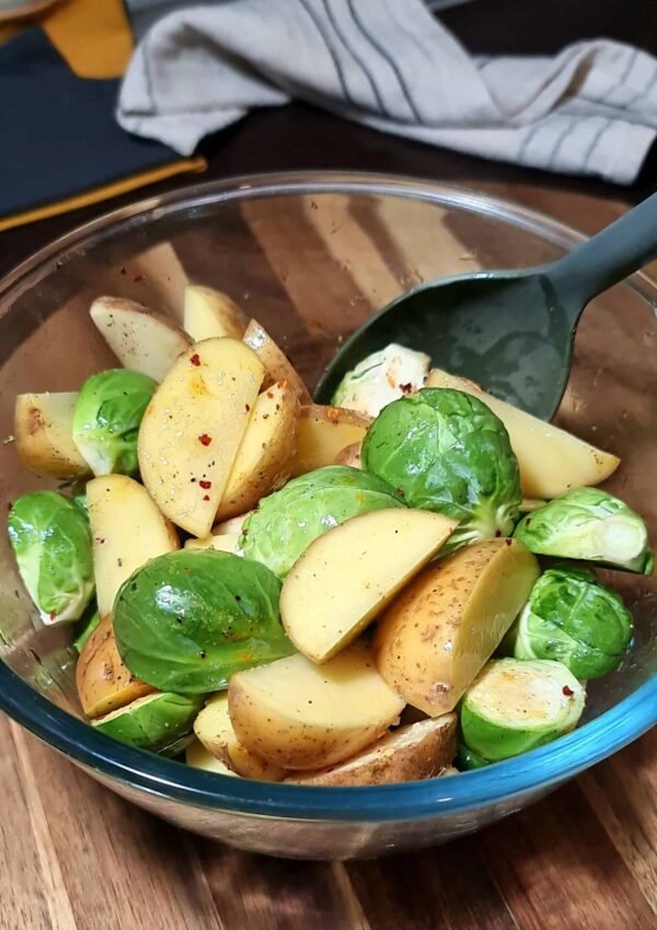 Fresh Brussels sprouts and potato wedges seasoned in a glass bowl before roasting.